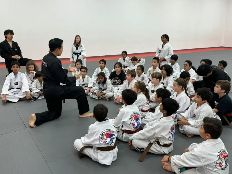 An instructor teaching a class of young students seated on the mat
