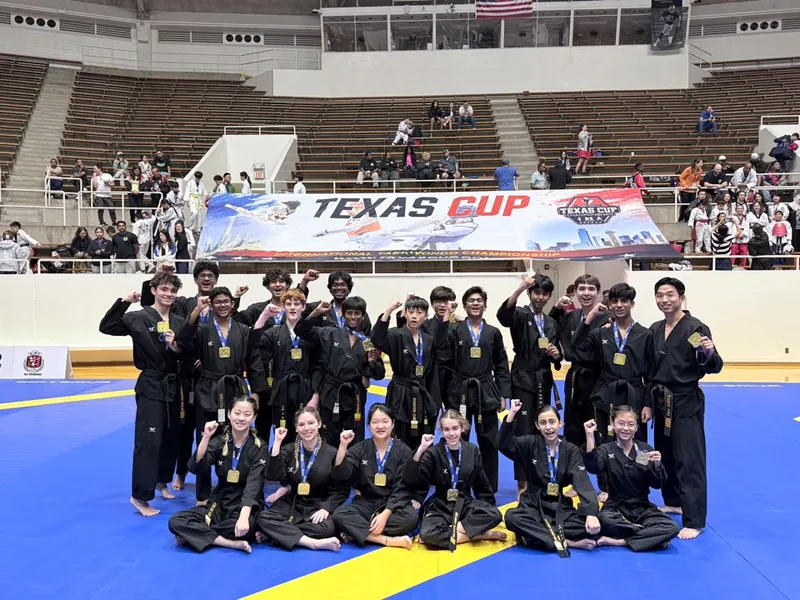 The Leaders Taekwondo Demo Team in black uniforms with gold medals in front of a Texas Cup banner