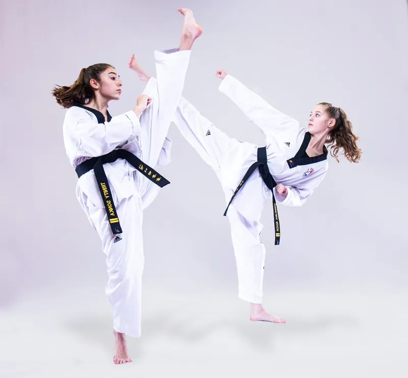 Two students in black belts throwing high kicks